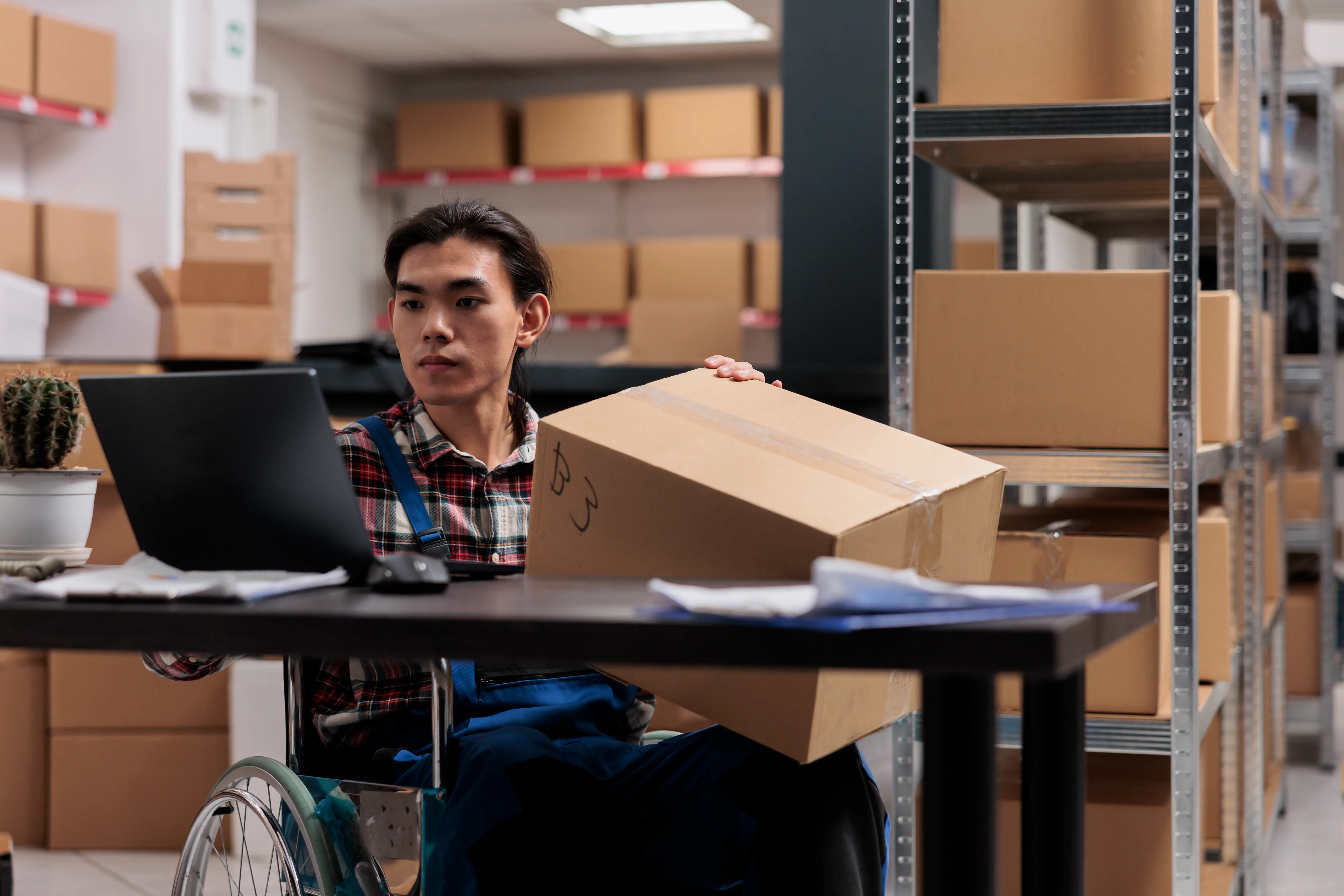 Warehouse worker checking a carton beside a computer and storage racks