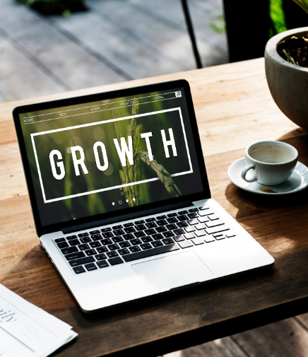Laptop displaying growth on a wooden desk with a newspaper, teacup, and flower vase
